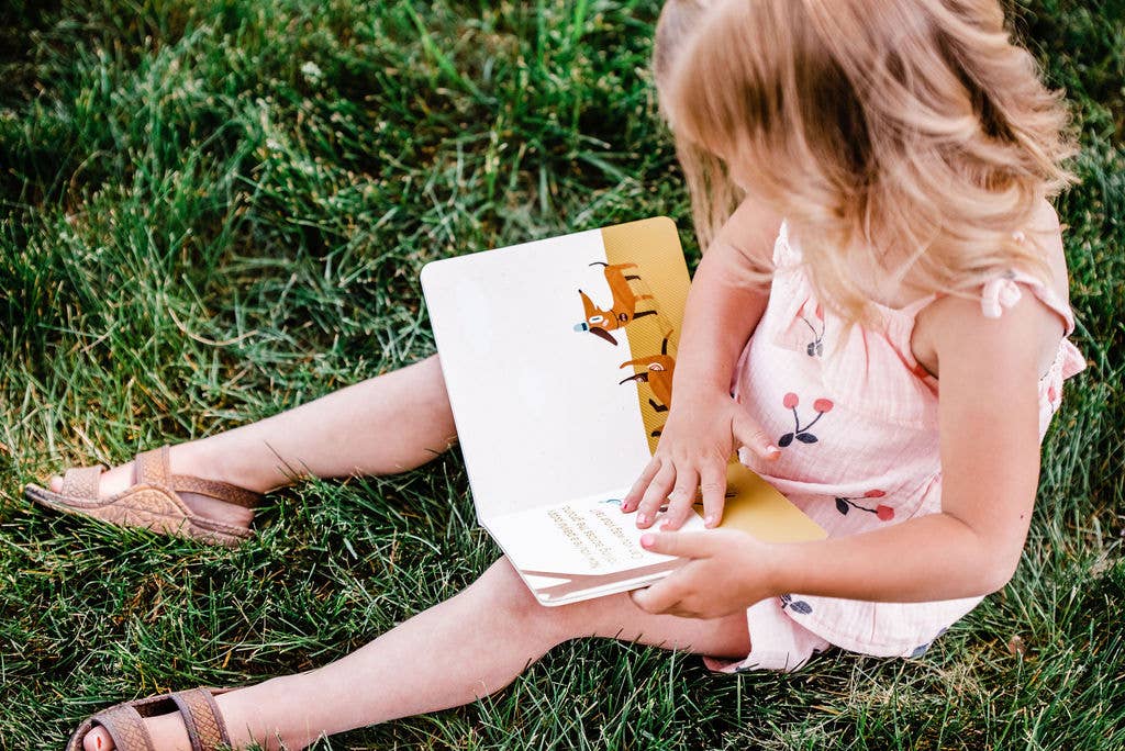 Little girl reading the board book outside.