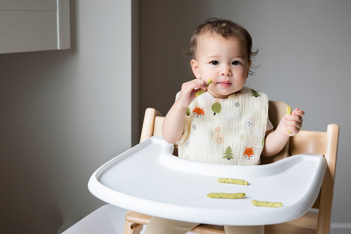 Baby wearing cotton muslin bib in fox and woodland print to keep clean.